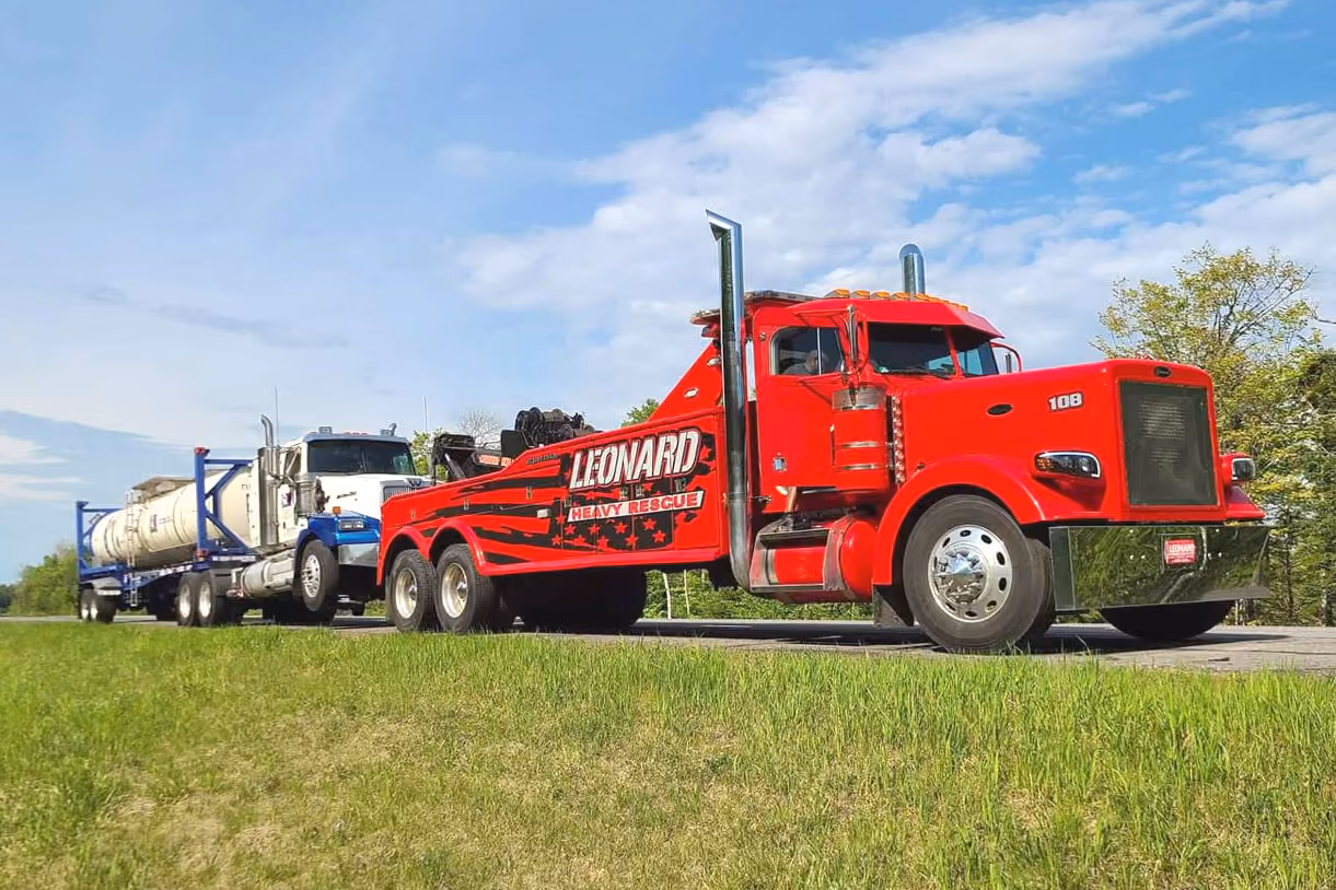 Red heavy rescue tow truck hauling a white tanker truck on a highway