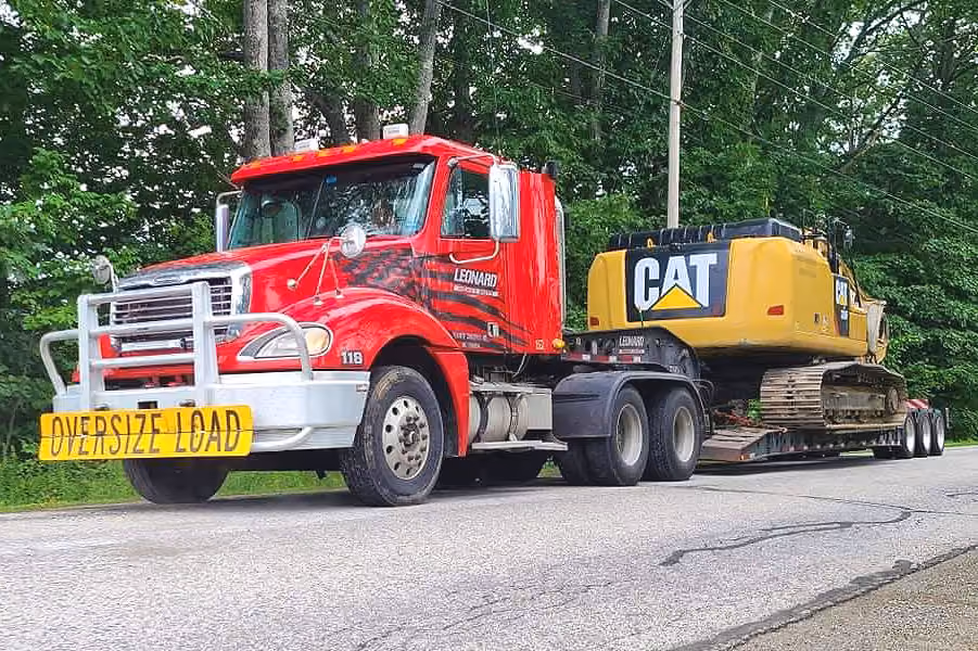 Red heavy-haul truck transporting a CAT excavator on a road.