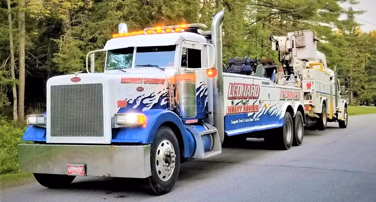 Heavy-duty tow truck with flashing lights parked on a wooded roadside.