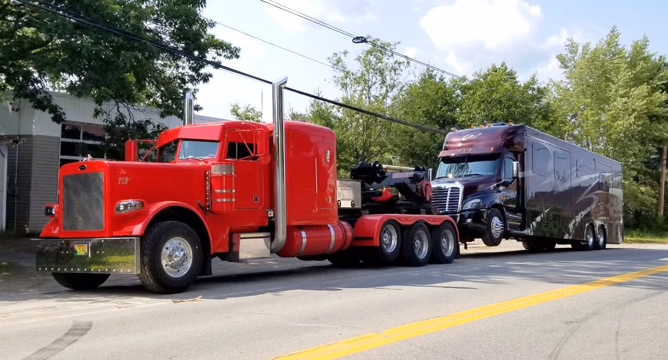 Red tractor truck hauling a black RV trailer beside a residential building.