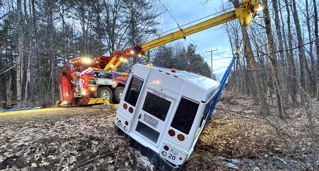 Recovery crew uses a crane truck to lift a bus off a roadside embankment.