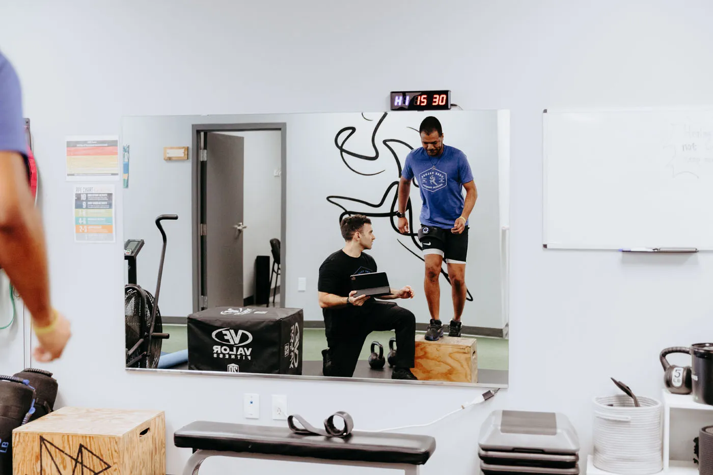 Physical therapist reviewing patient movement on an iPad reflected in a gym mirror