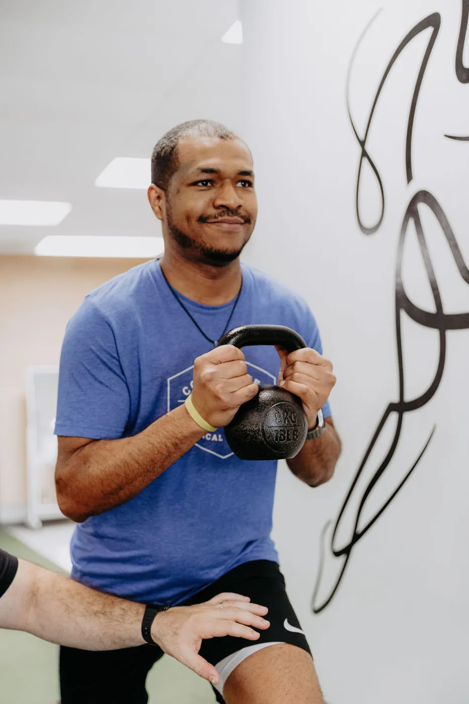 Patient performing a kettlebell squat under physical therapist supervision