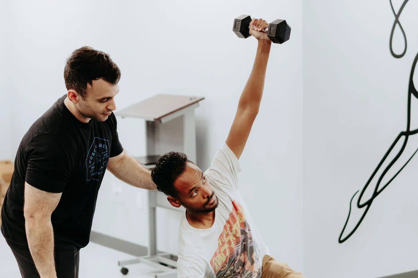Physical therapist assisting a patient with an overhead dumbbell exercise