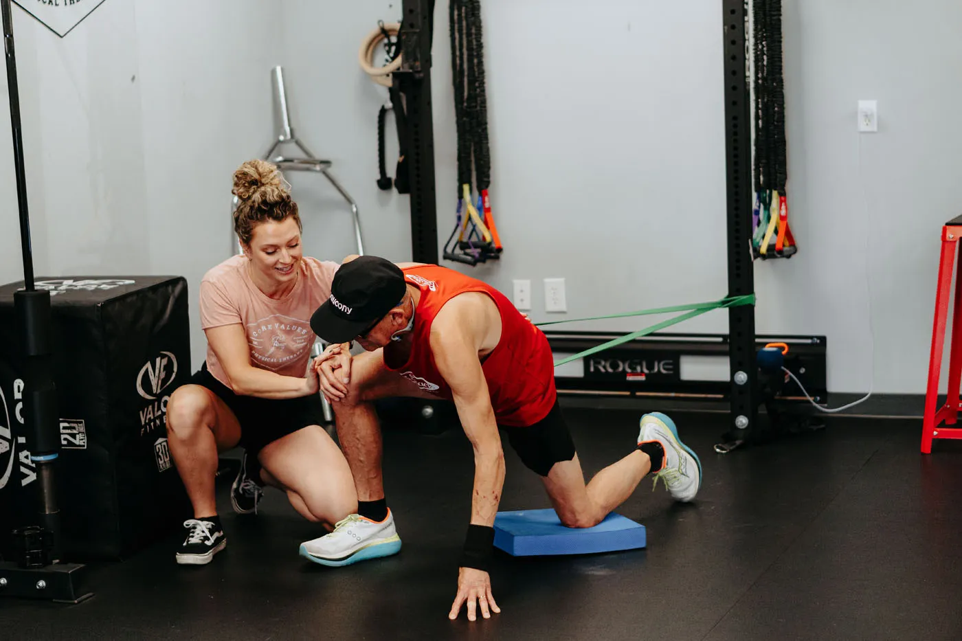 Physical therapist coaching a patient on a balance pad near Rogue equipment