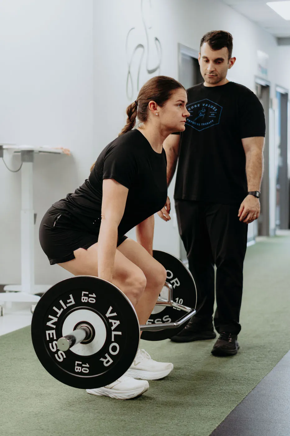 Patient performing a barbell deadlift supervised by a physical therapist