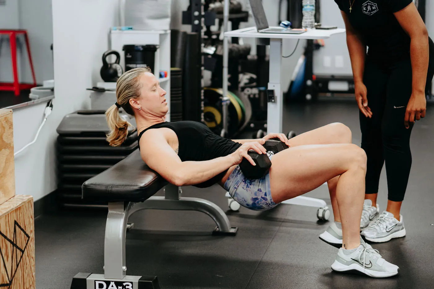 Patient performing a hip thrust exercise with a physical therapist standing by