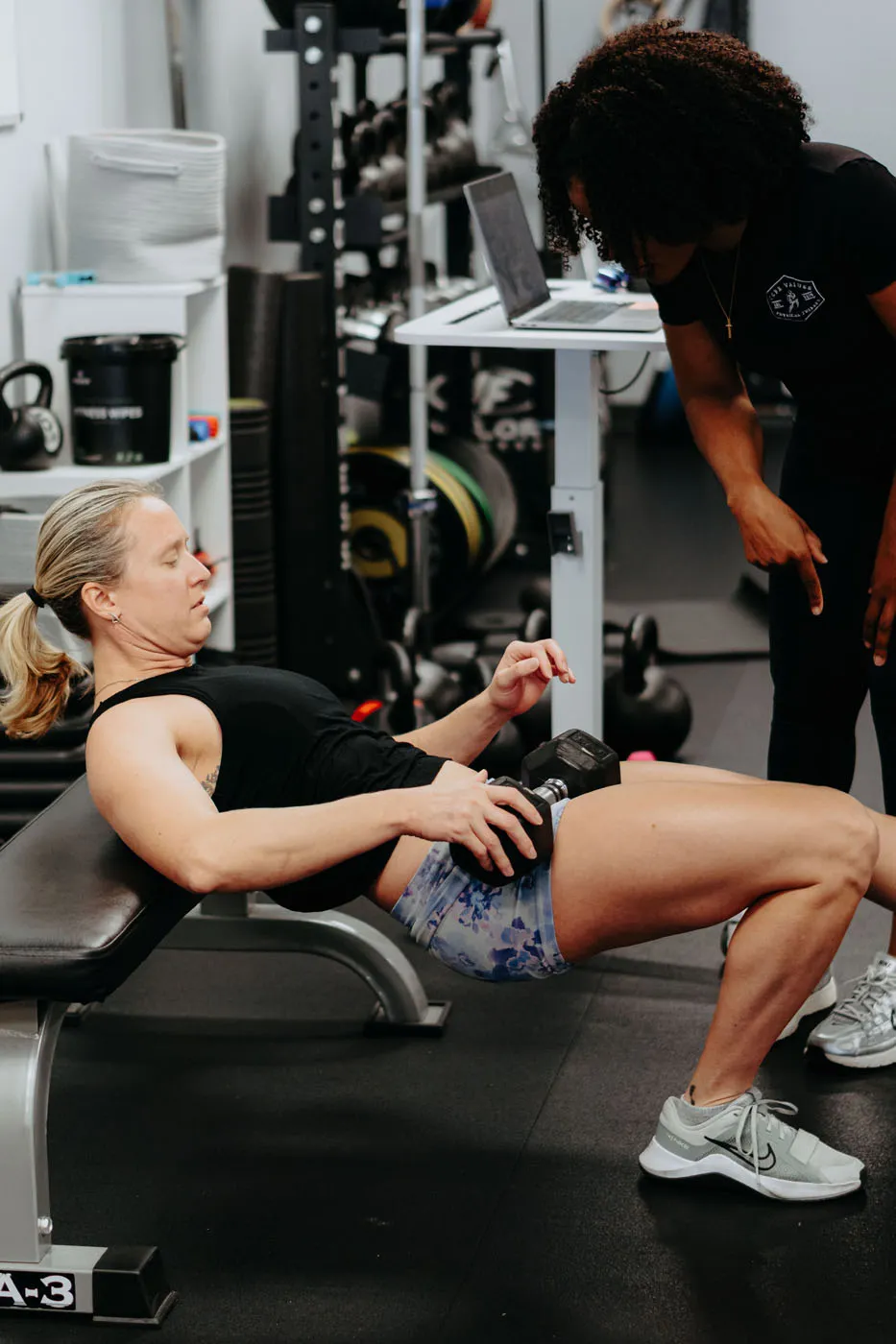 Patient performing a dumbbell hip thrust on a bench under physical therapy supervision