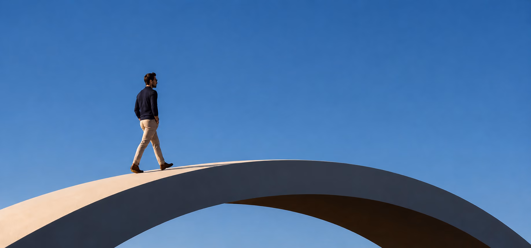 Homem caminhando sobre uma ponte em arco sob céu azul