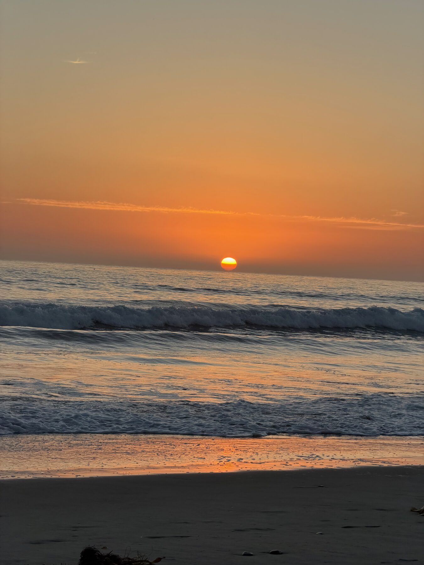 The sun setting into the Pacific, seen from the wet sand at low tide