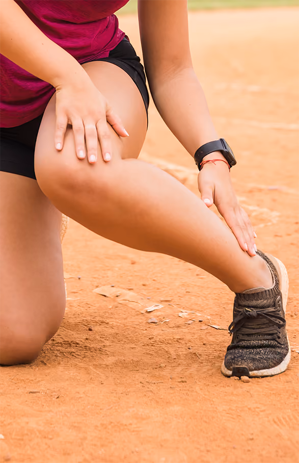 Persona con ropa deportiva tocando su pierna, aparentemente con dolor o molestia.