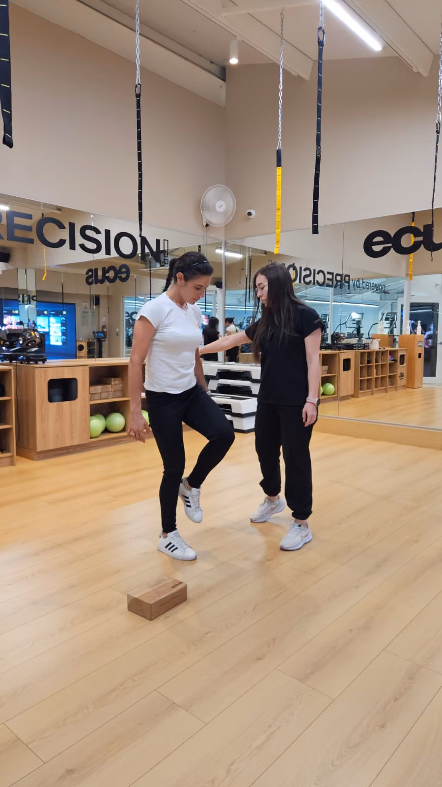 Entrenadora ayuda a mujer a hacer ejercicio de equilibrio levantando una pierna en gimnasio.