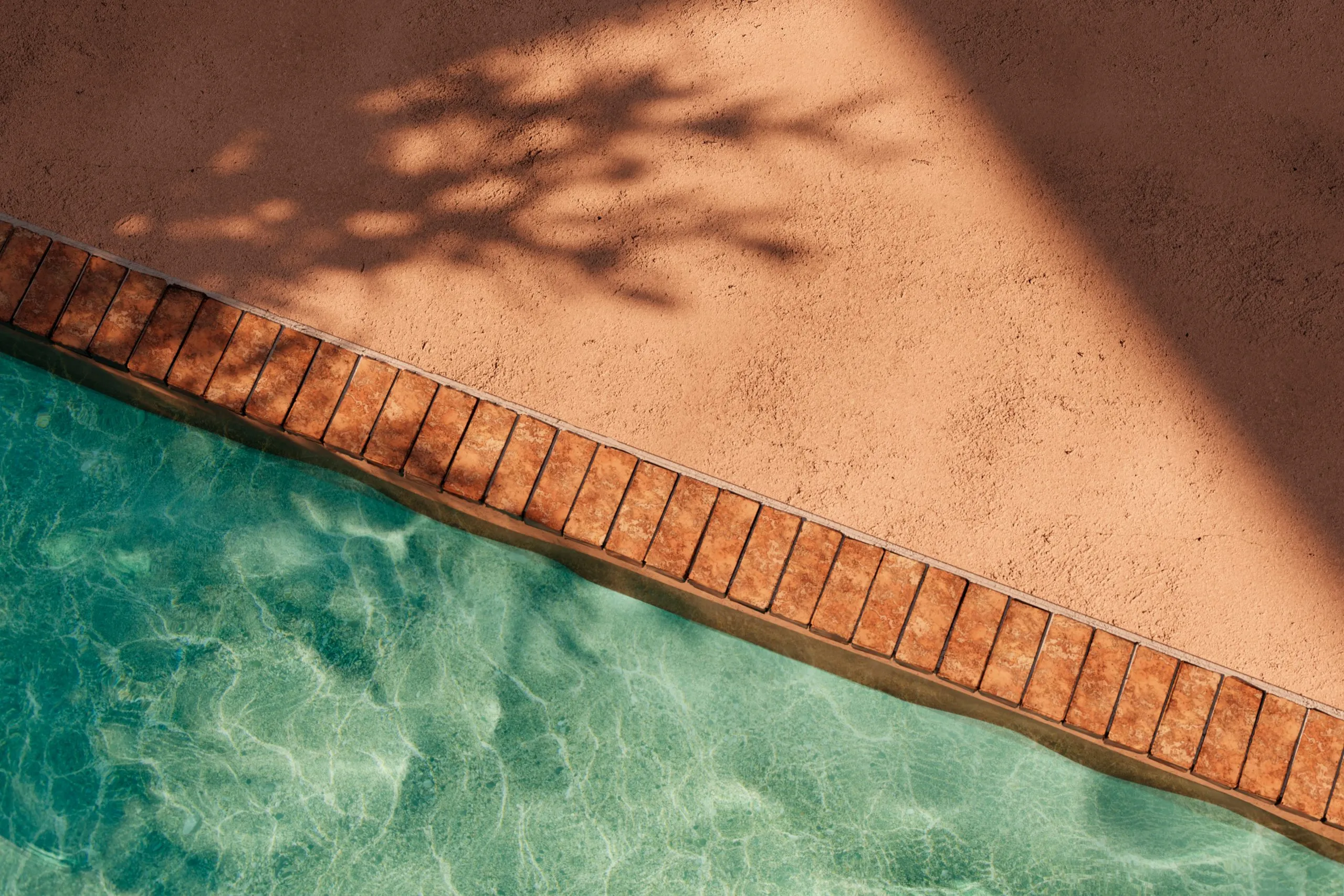 Turquoise water in a pool with reflections beside a terracotta tile border and stucco deck with shadows.