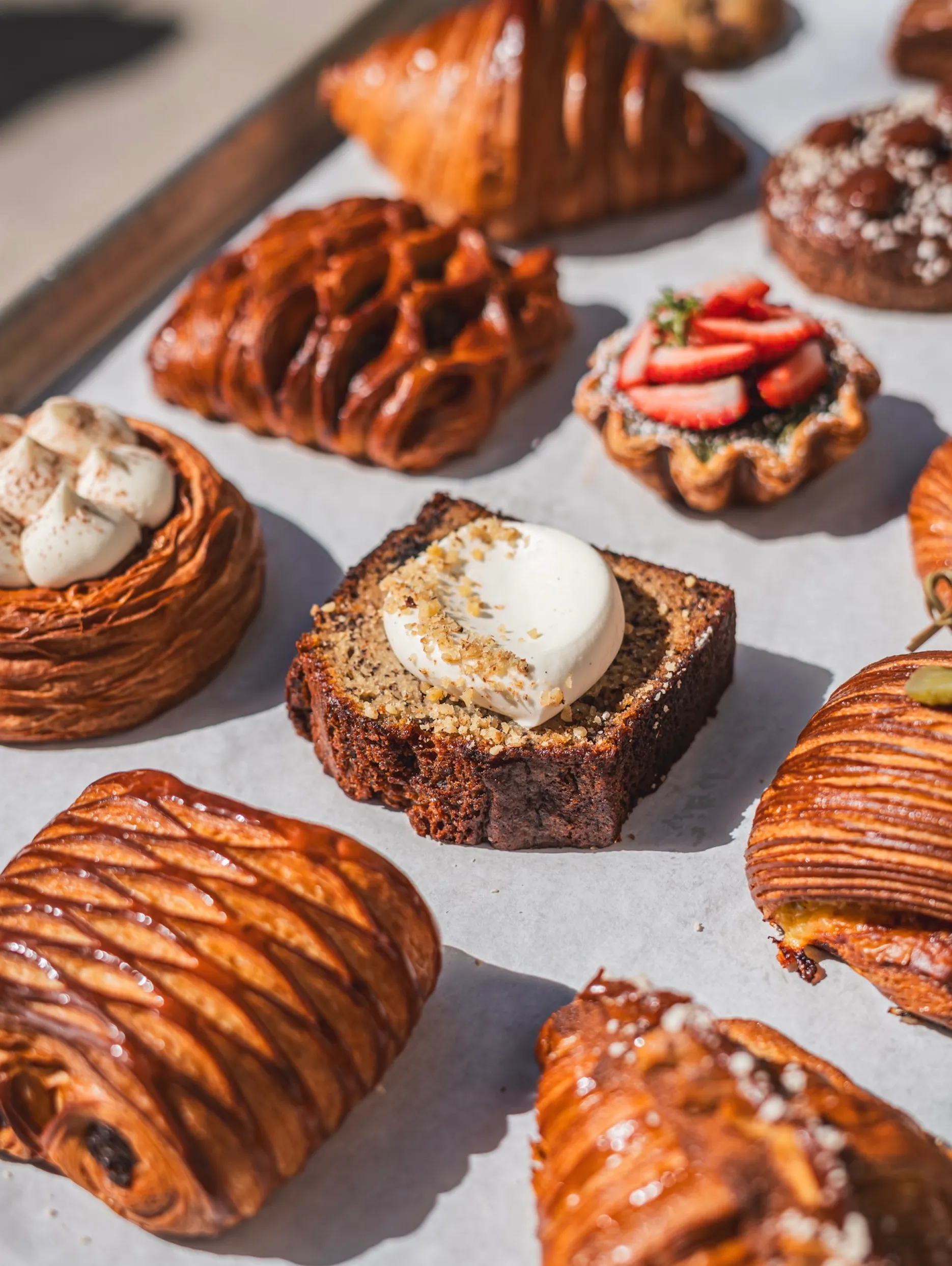 Assorted pastries on parchment including a slice of nut bread with cream and strawberry tart.