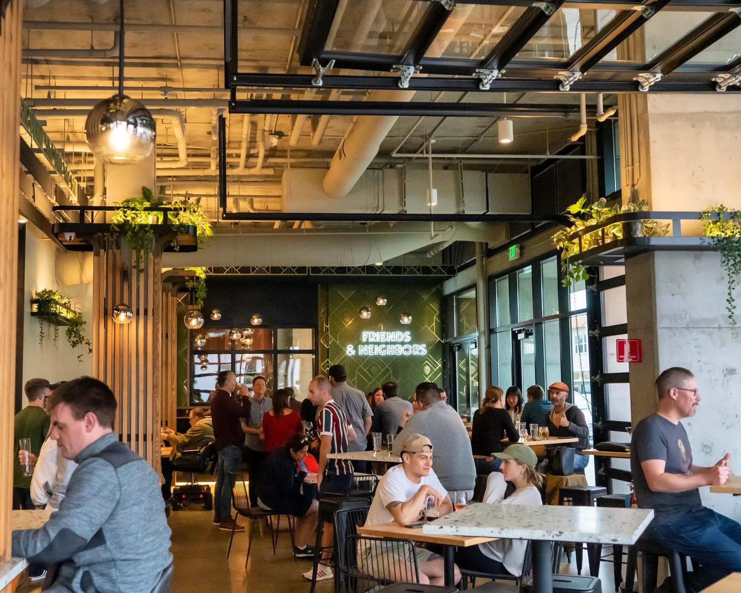 People sitting and chatting in a modern, plant-decorated café under a sign reading Friends & Neighbors.