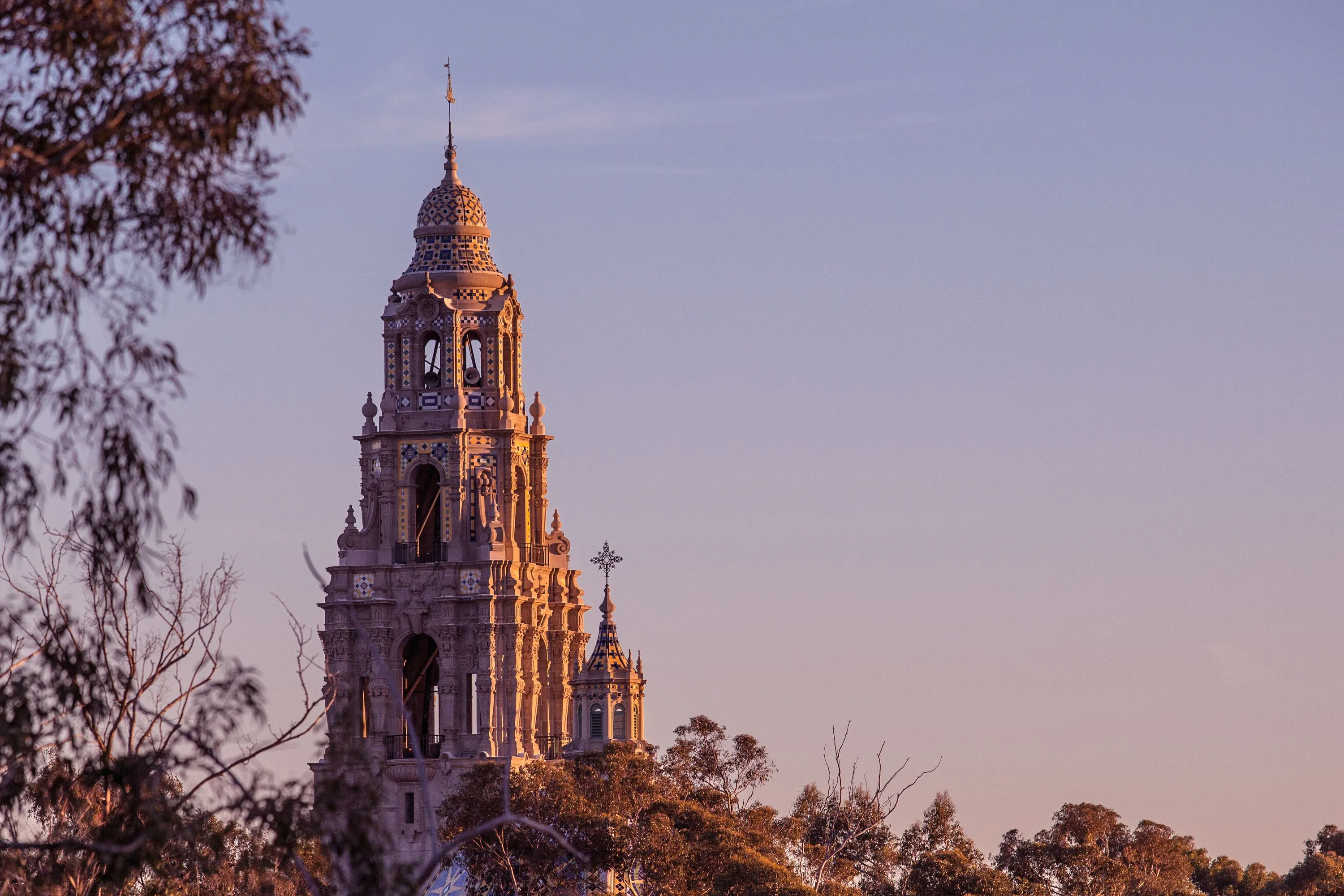 Ornate bell tower of a historic building bathed in warm sunlight with trees in the foreground.