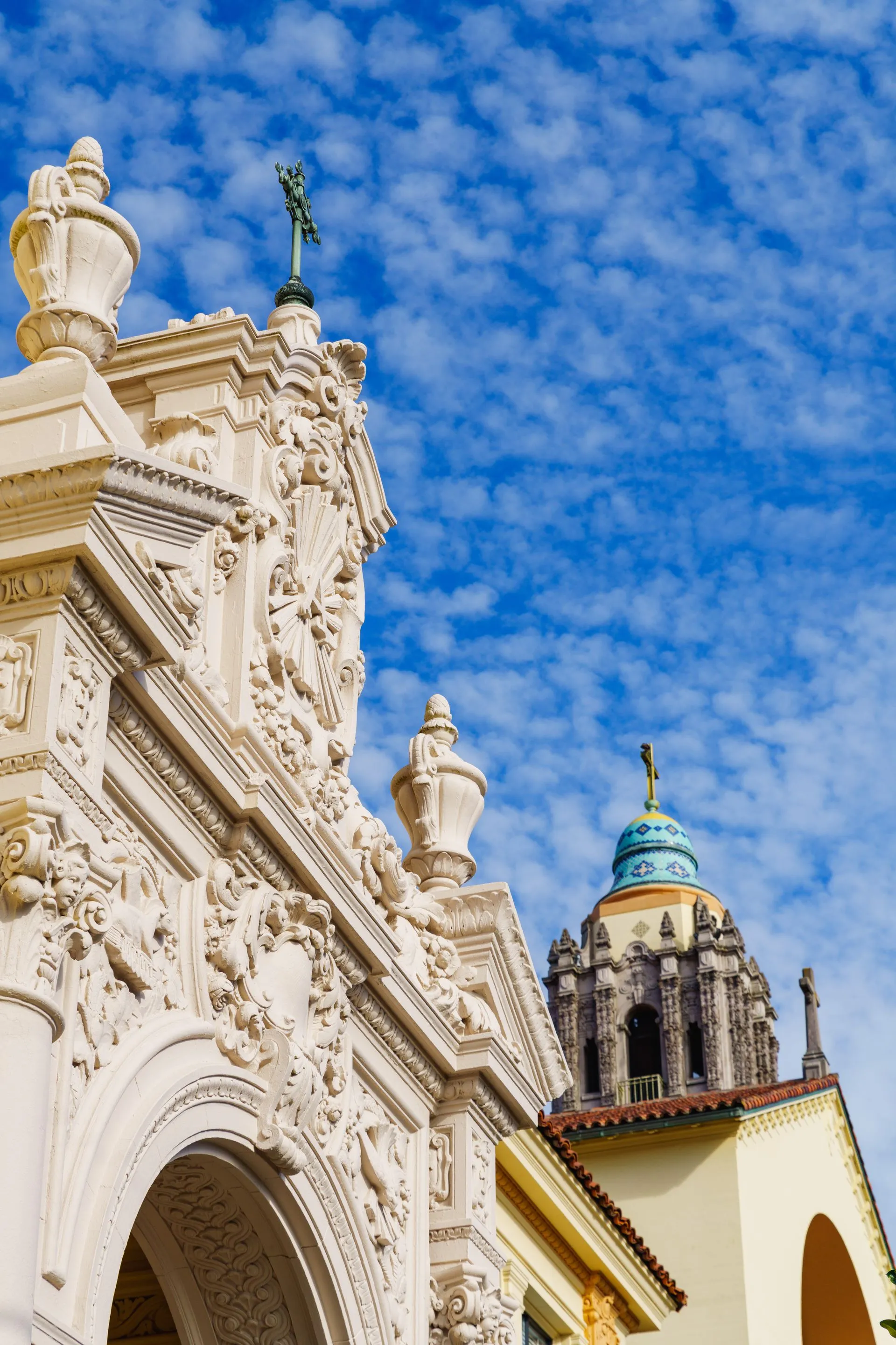 Ornate white stone church facade with a blue-domed tower under a partly cloudy sky.