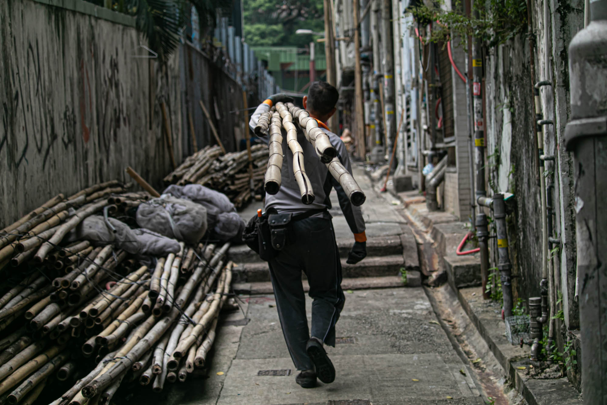 Worker carrying bamboo through a Hong Kong alley