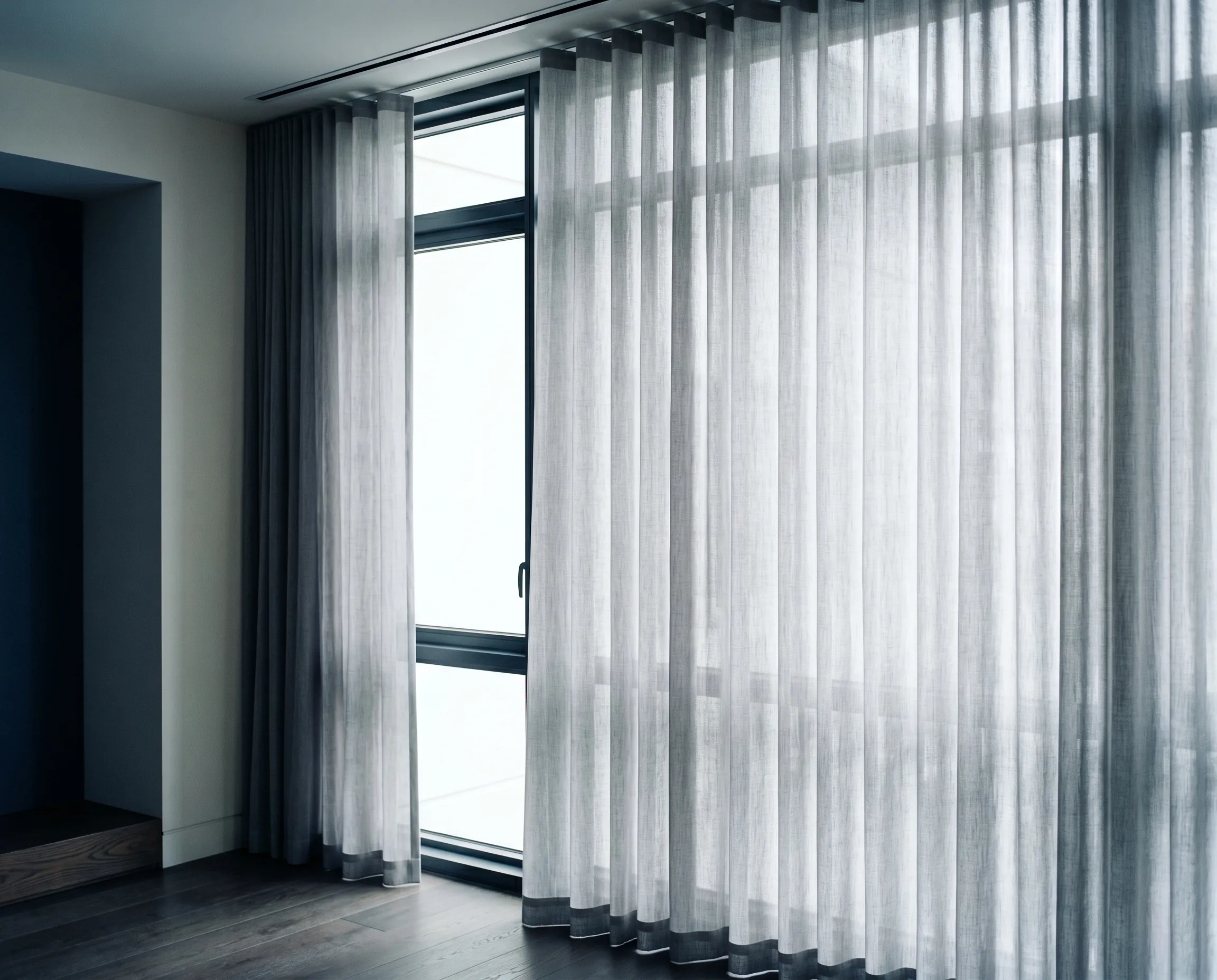 Transparenter grauer Vorhang bedeckt große Fenster in modernem Raum mit Holzboden.