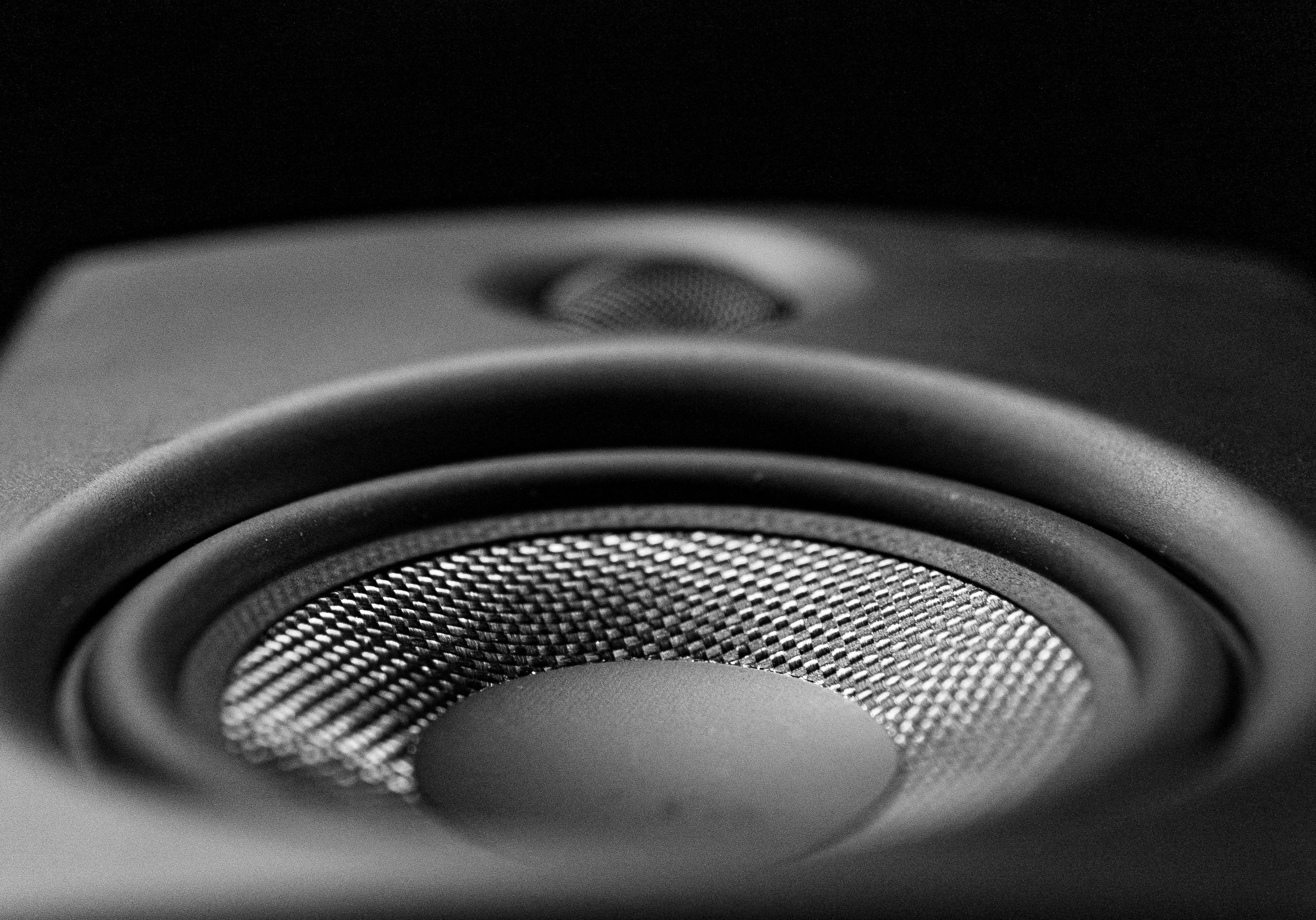 Close-up of a black speaker cone with woven texture and a small tweeter above it against a dark background.