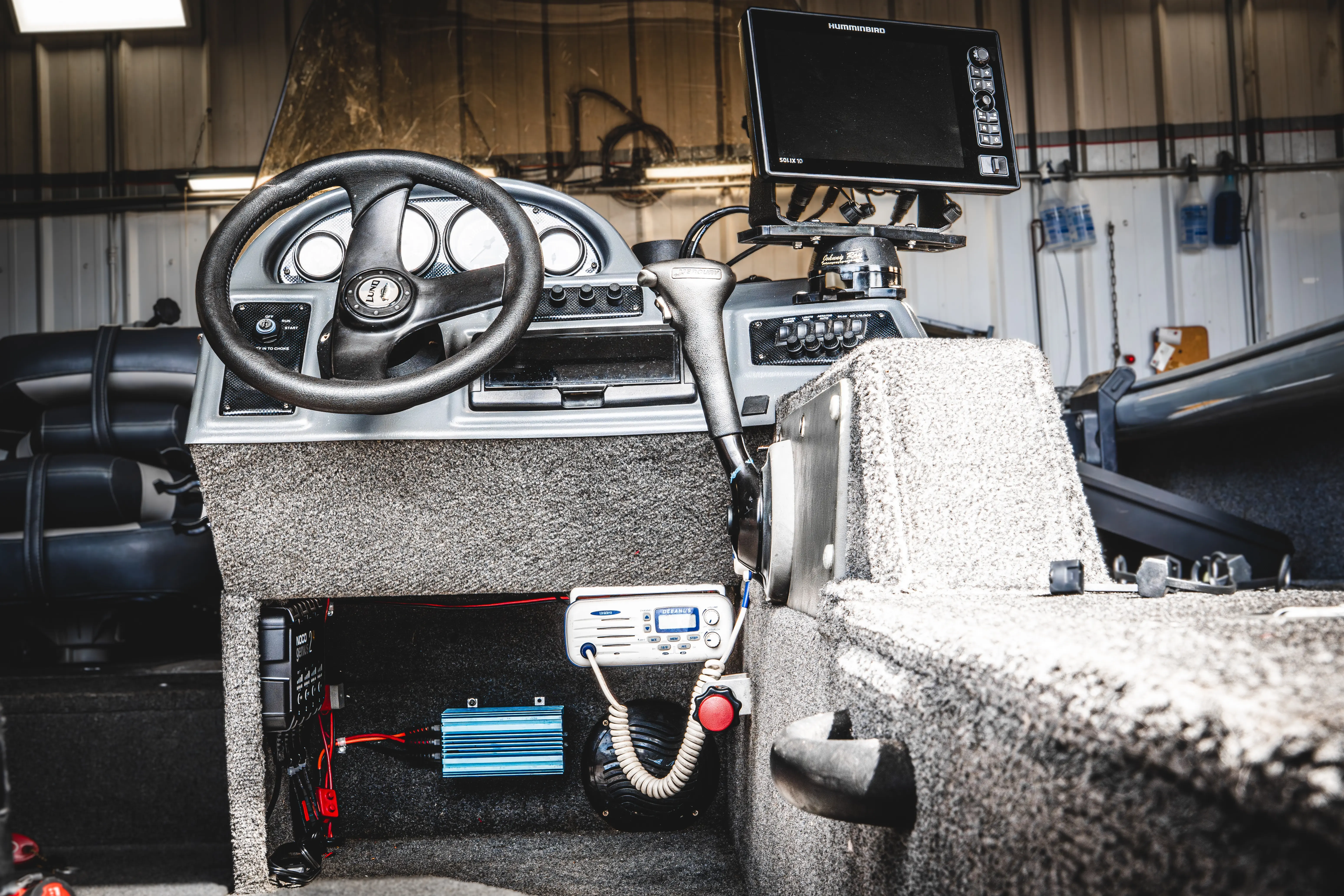 View of a boat's cockpit showing steering wheel, control lever, and mounted fishfinder screen.