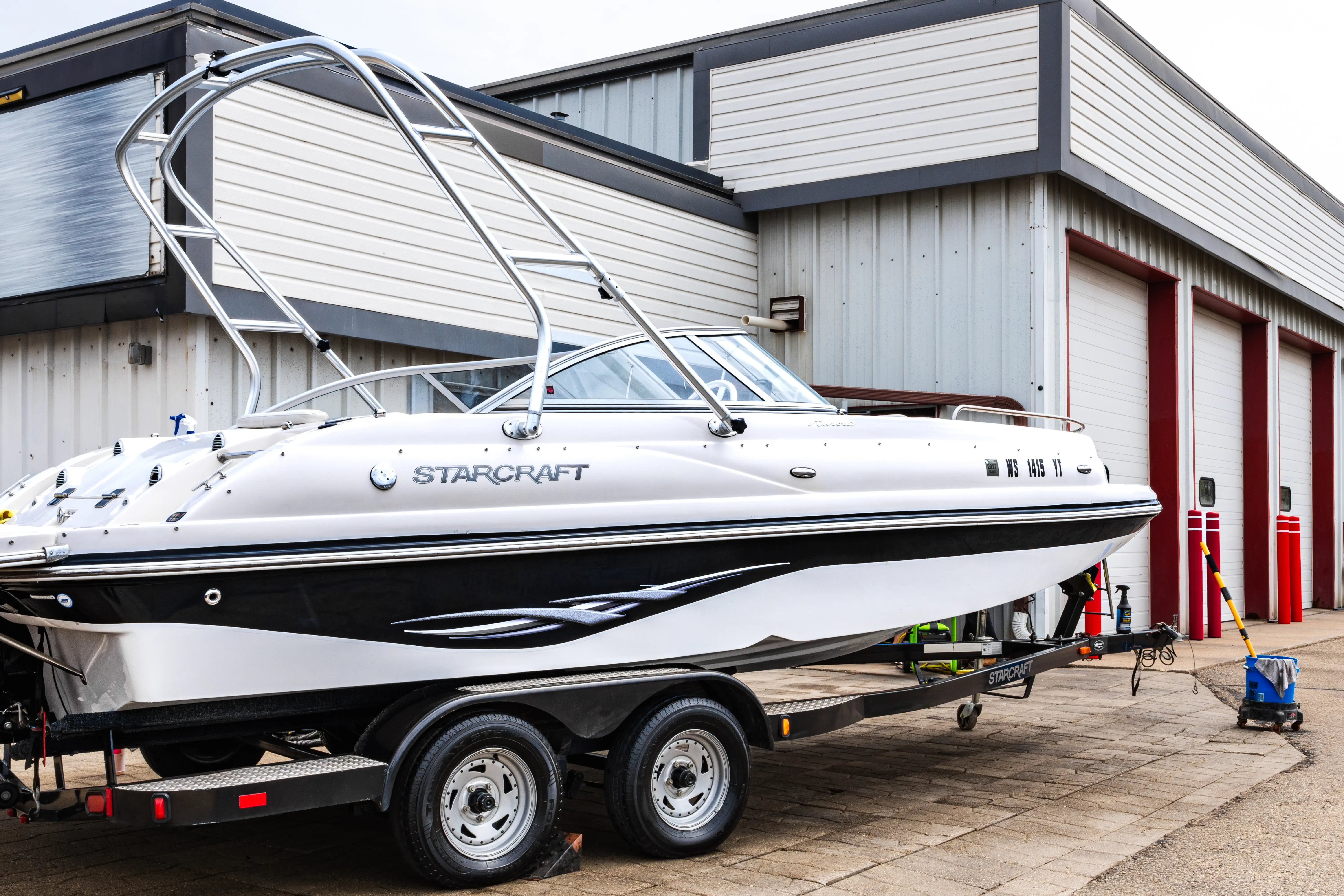 White and black Starcraft motorboat on trailer parked outside a building with garage doors.