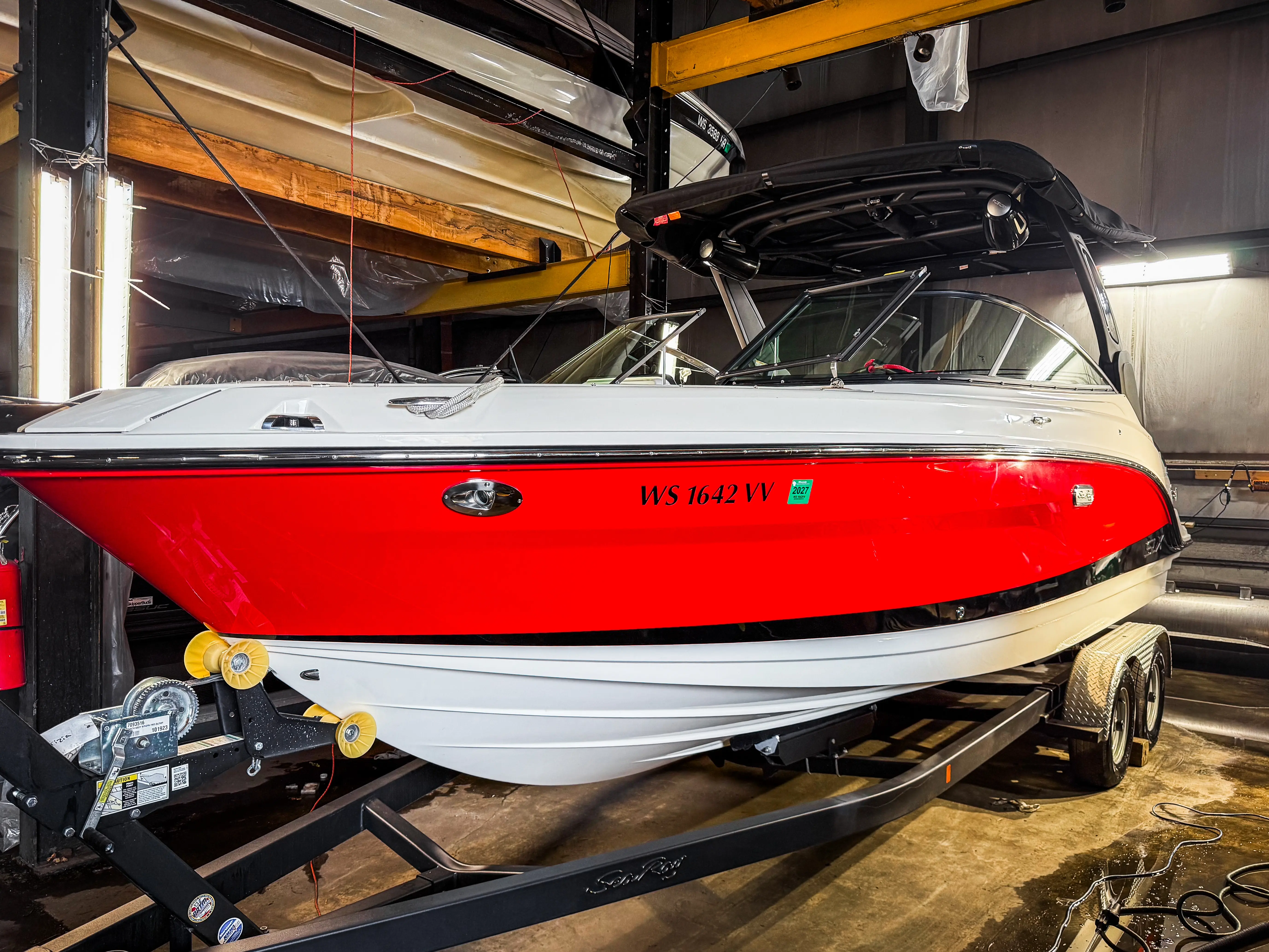 Red and white motorboat with black canopy on a dual-axle trailer inside a garage.