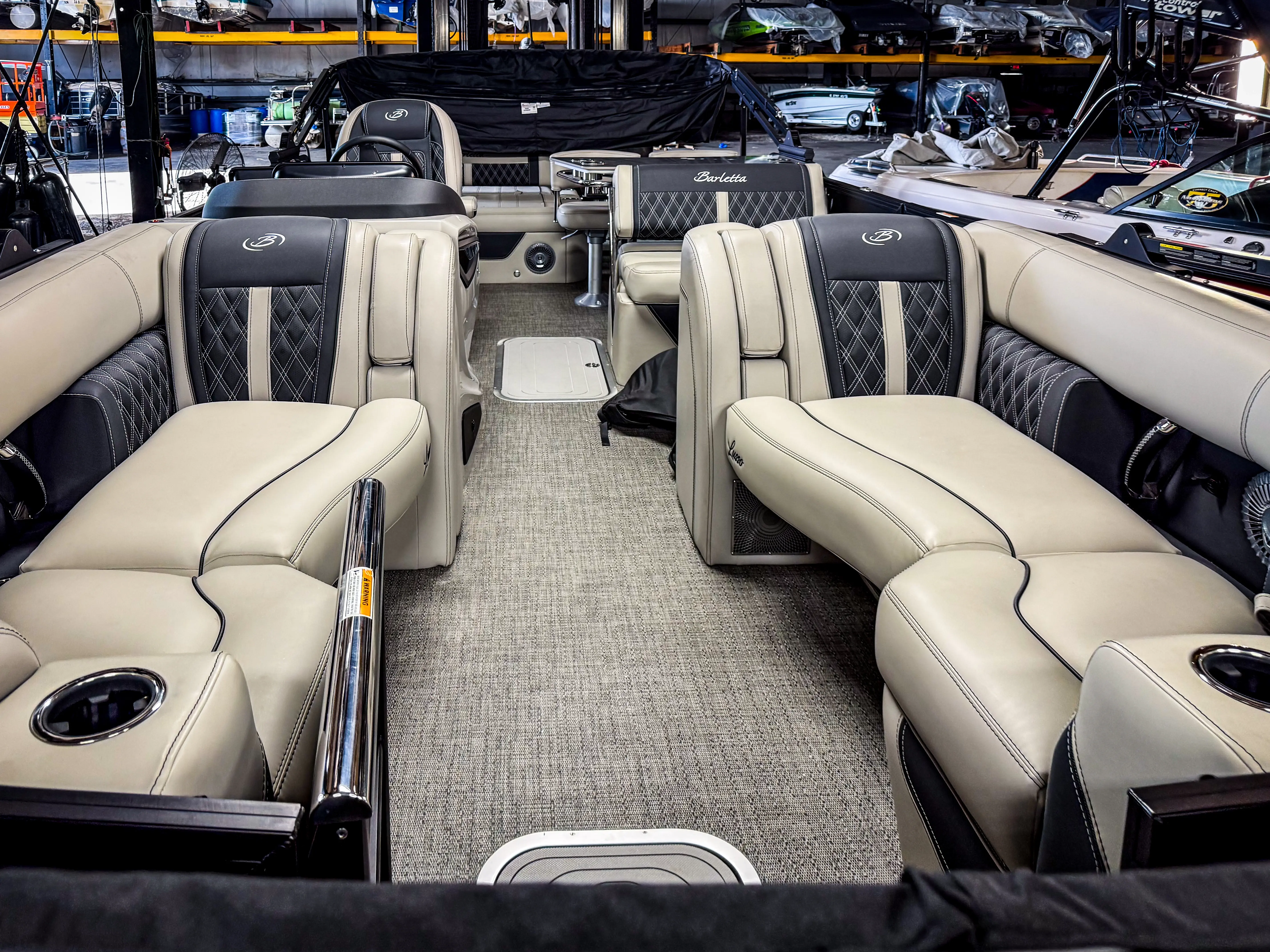 Interior of a luxury pontoon boat with beige and black cushioned seats and a central aisle.