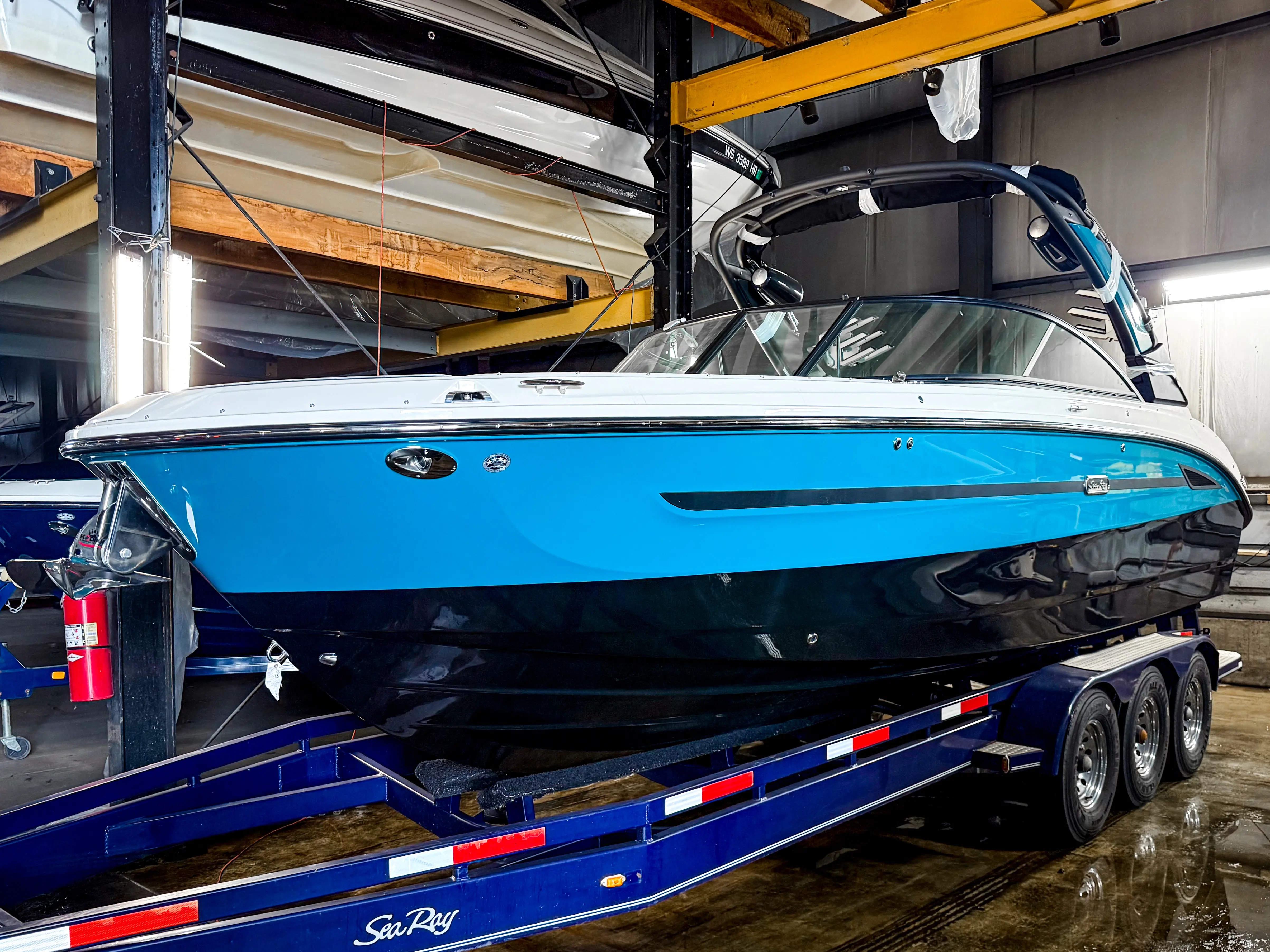 Blue and black Sea Ray boat on a triple-axle trailer inside a warehouse with wood beams.
