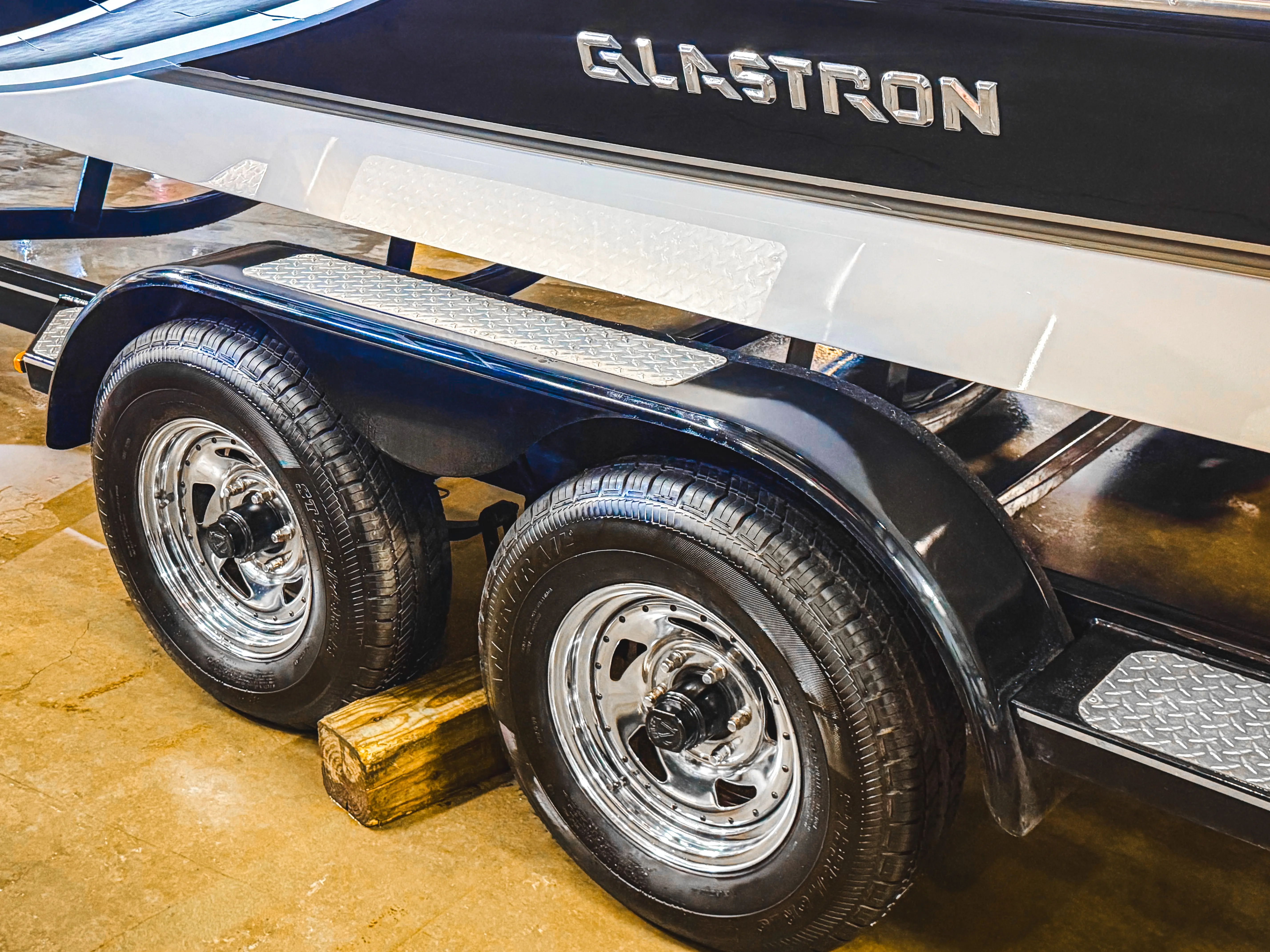 Close-up of a boat trailer's dual tires under a black and white boat with Elastron branding.