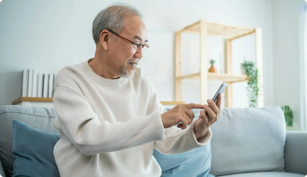 Older adult using a smartphone while sitting on a couch at home.