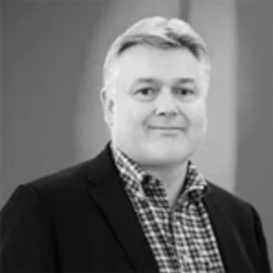 Black-and-white professional headshot of a man wearing a blazer and checkered shirt.