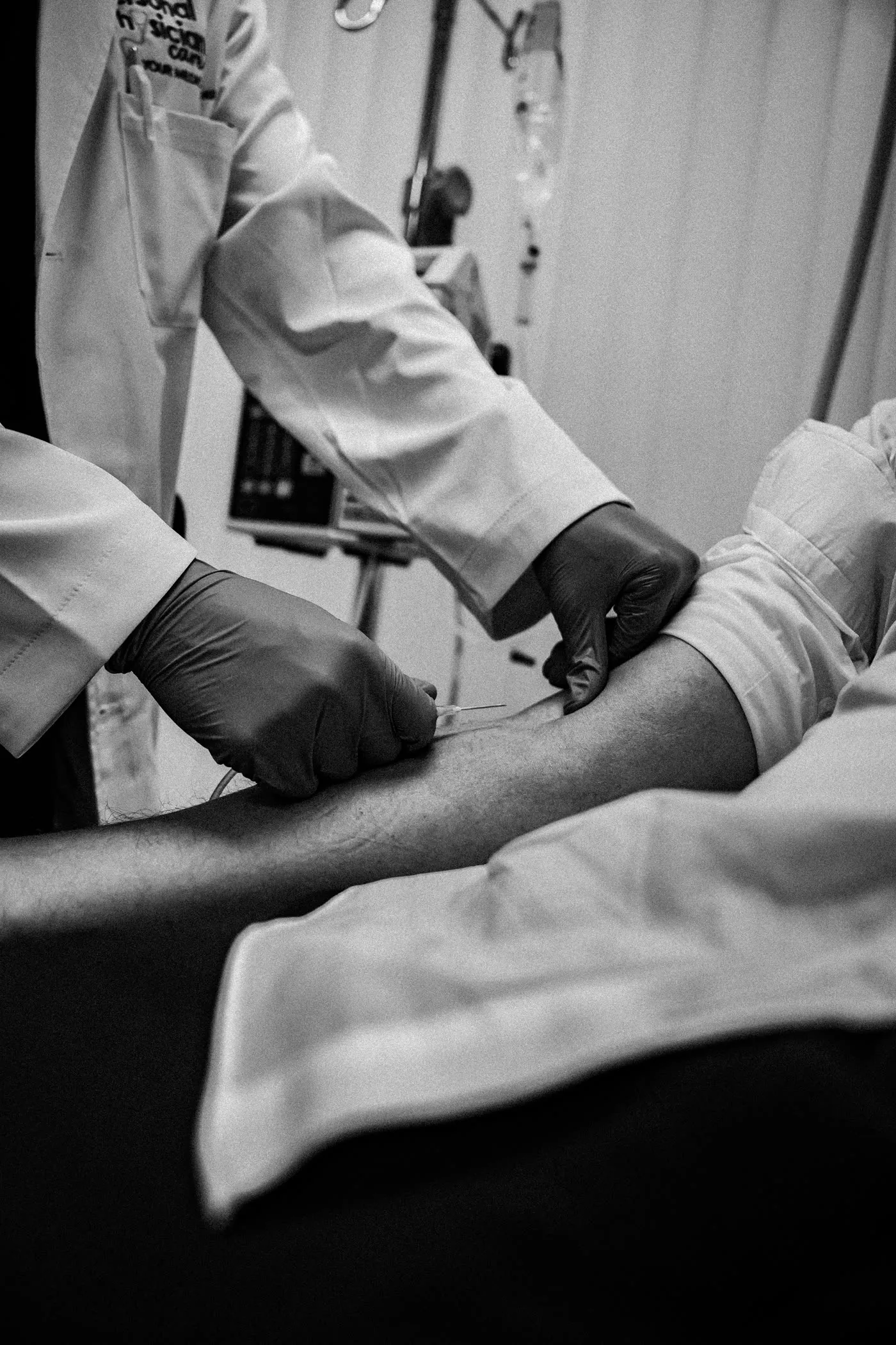 Gloved hands drawing blood from a person's arm, shown in black and white