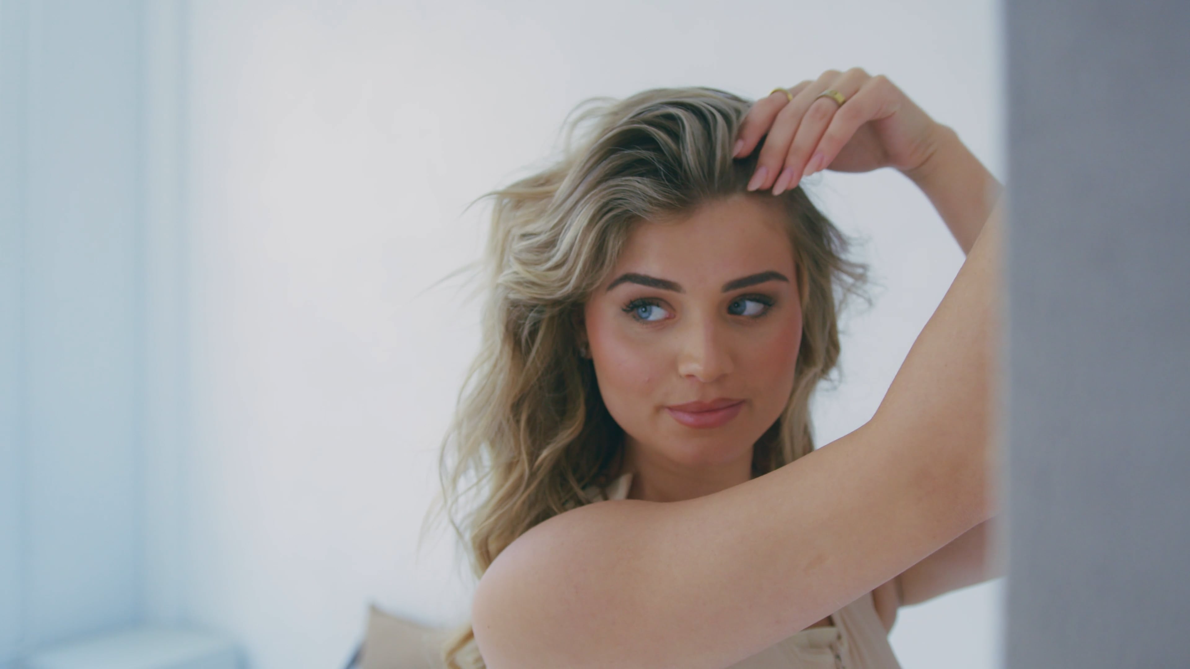 Blonde model running a hand through her hair in a soft-lit studio, AfterSurgery campaign
