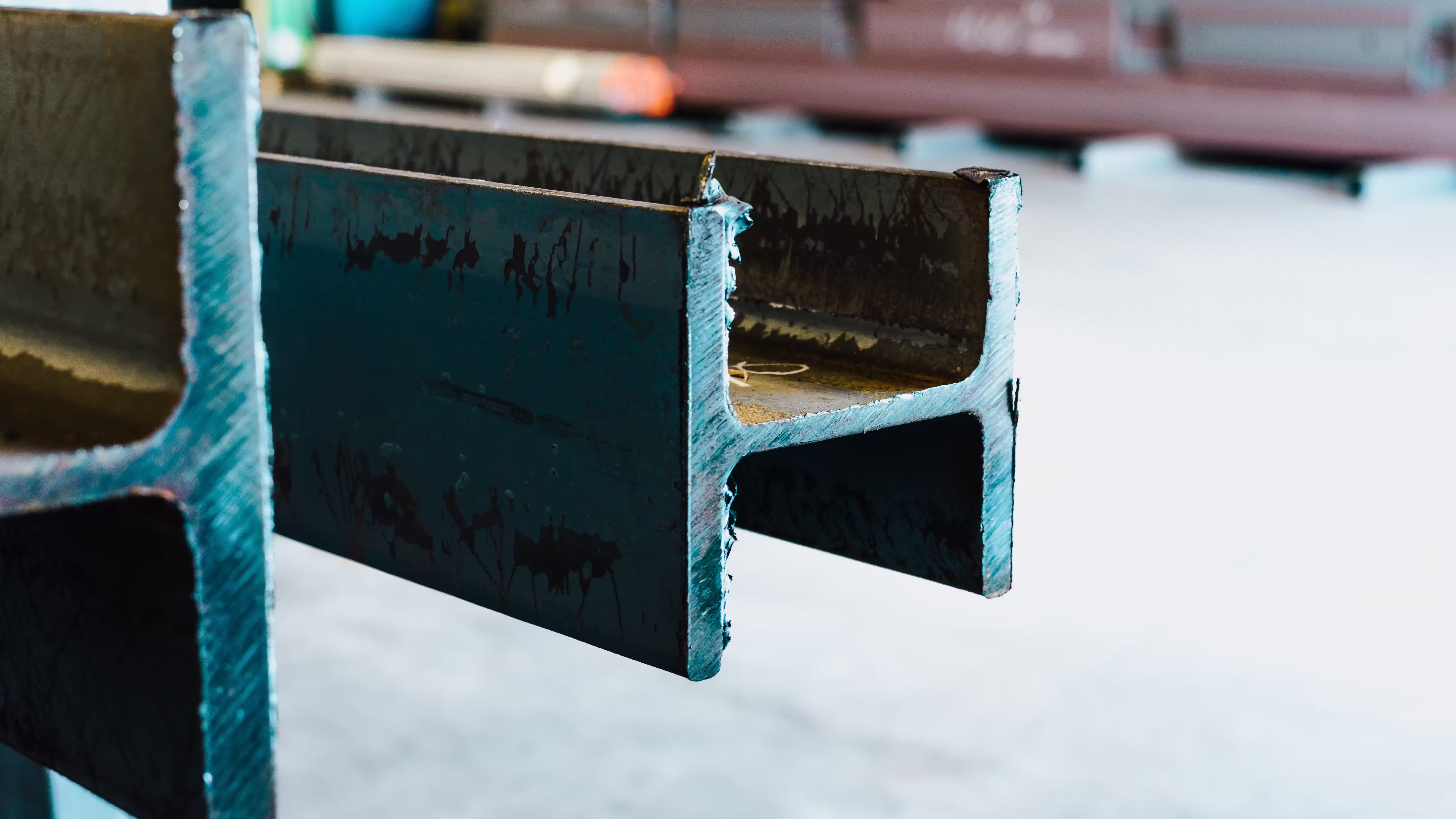 Two steel beams with a green-blue finish on a workshop floor