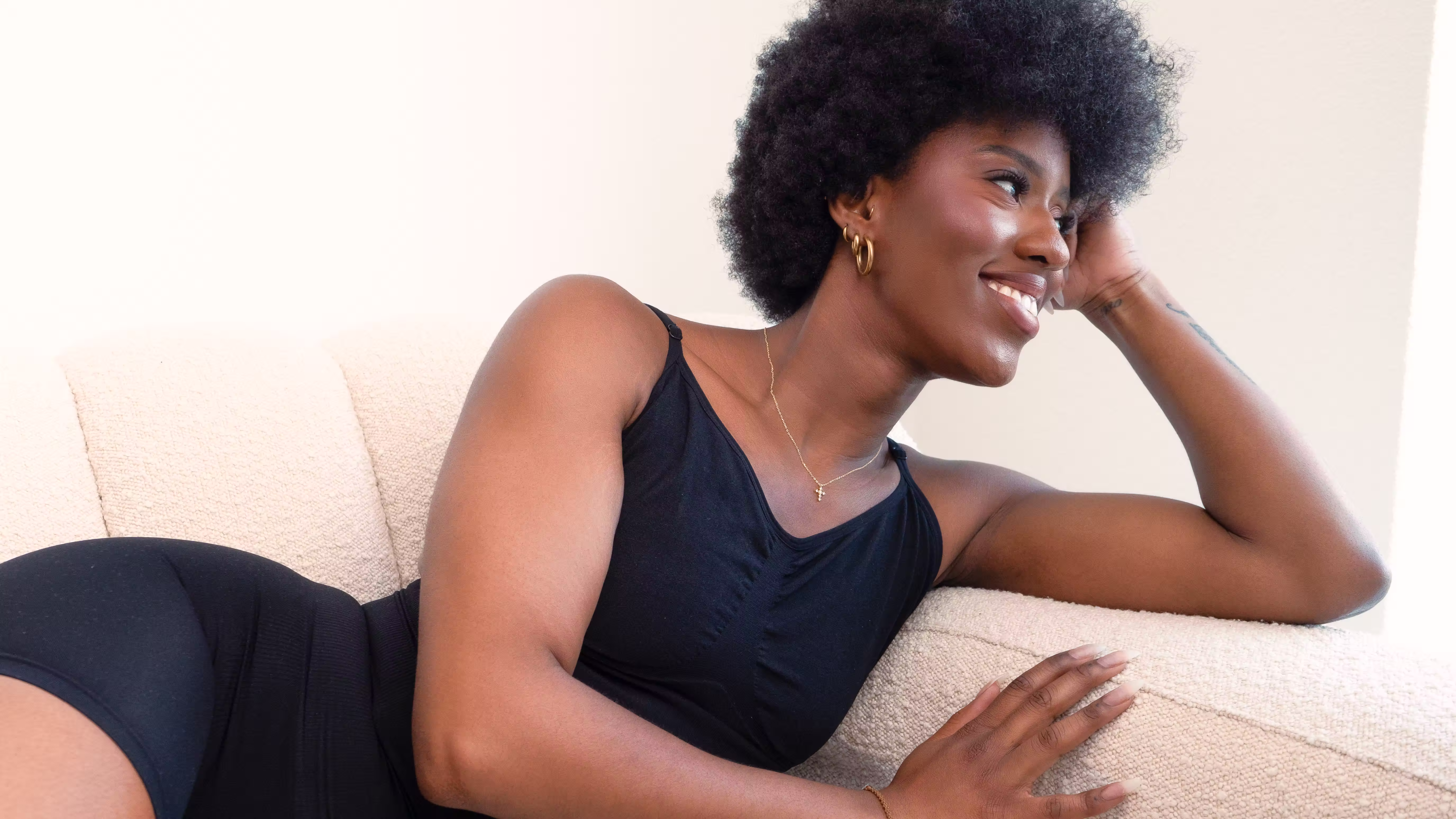 Smiling woman in a black Essie compression top reclining on a sofa
