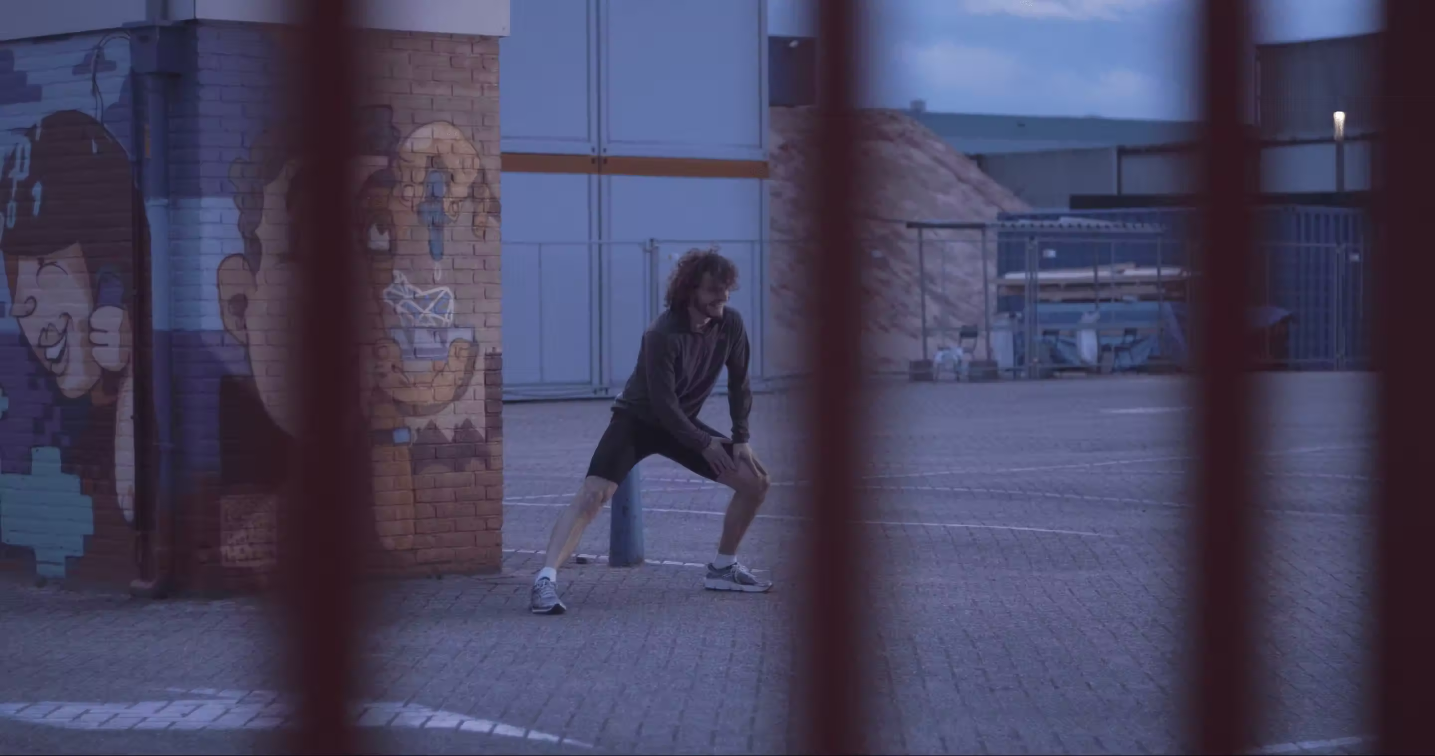 Athlete stretching in an urban yard, viewed through railings