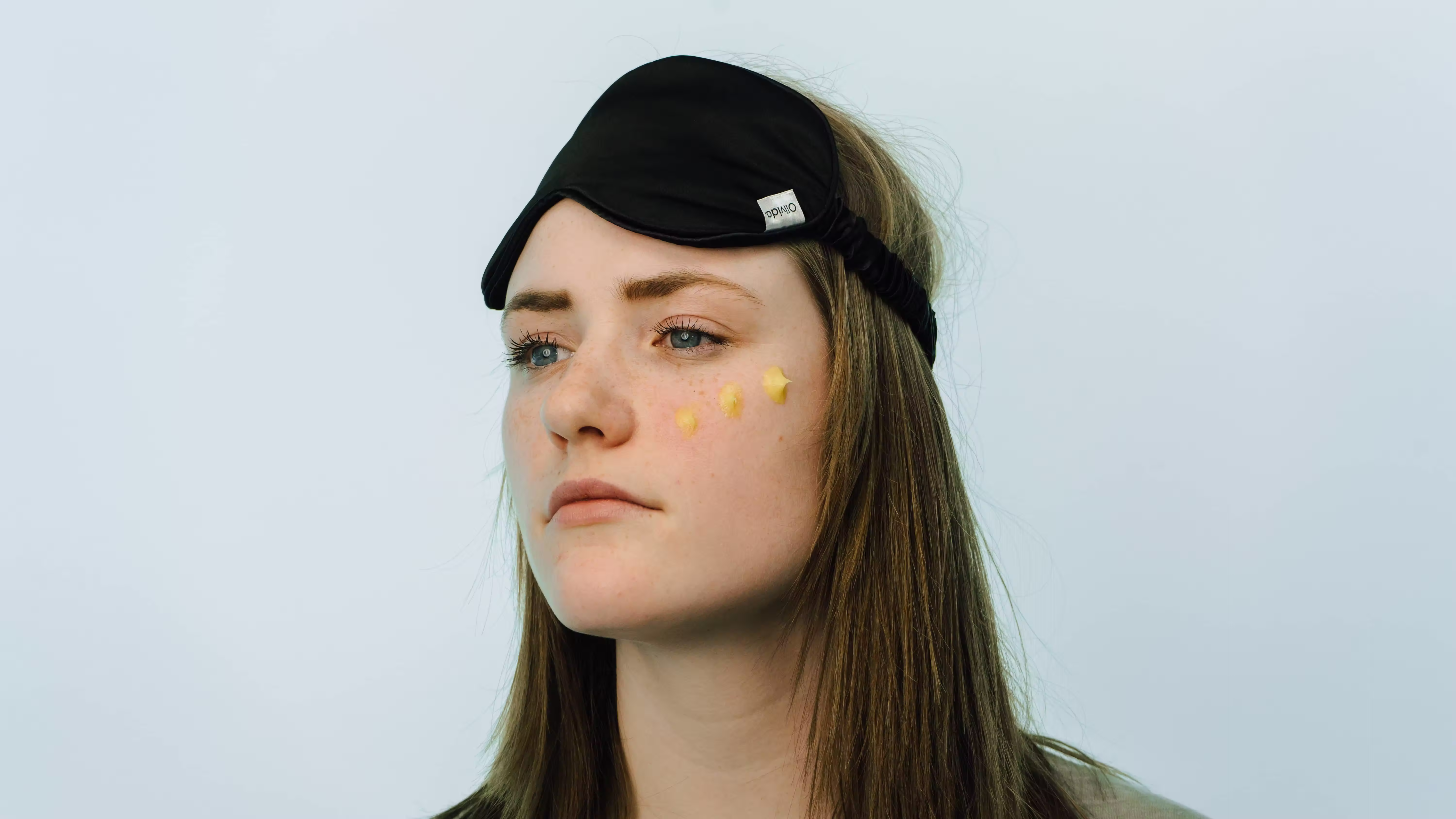 Young woman in a headband with yellow skincare product dots on her cheek, Olivida