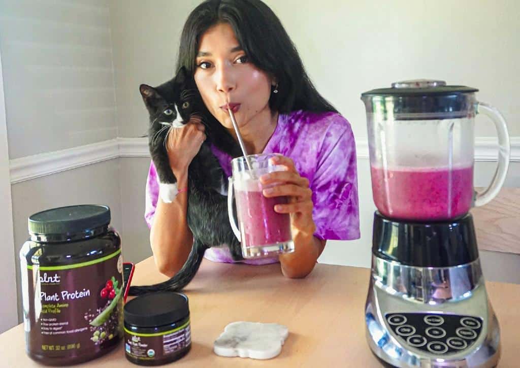Lina Mayorga hugging kitten while drinking plant protein shake