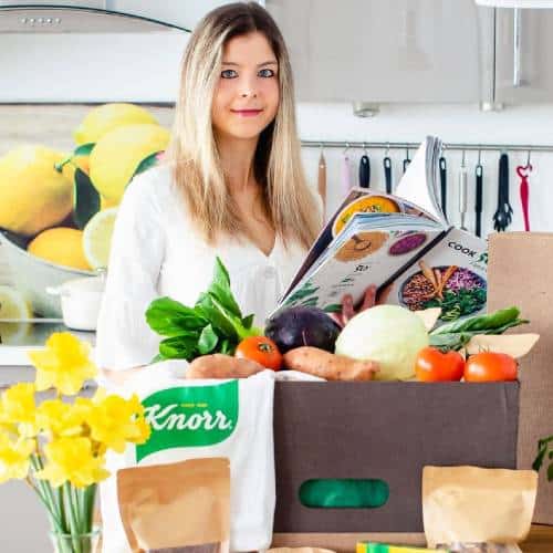 Bianca Zapatka | Reading a recipe book with bags of veg on the side