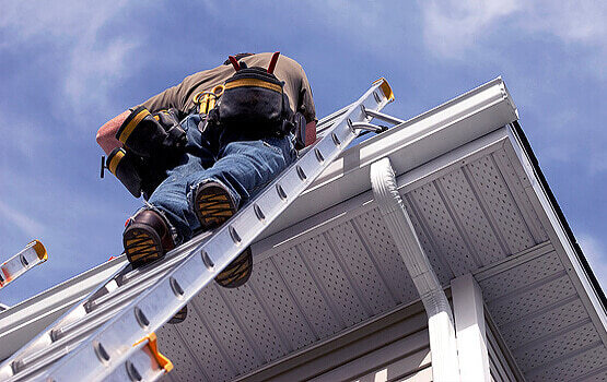 A roof inspector on a ladder examining a home’s gutter line