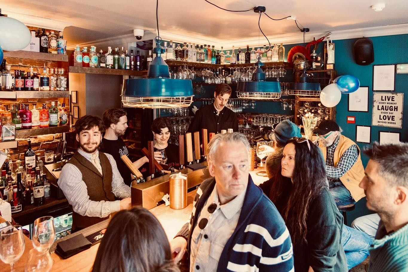 Interior of Kaldi Craft Bar in Reykjavik, capturing patrons enjoying drinks in a cozy, warmly-lit setting with an extensive selection of spirits and beers.