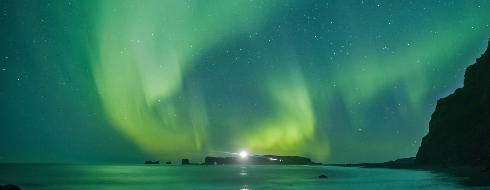Reynisfjara Black Sand Beach with Northern Lights in Green dancing above on a dark winter night in Iceland.