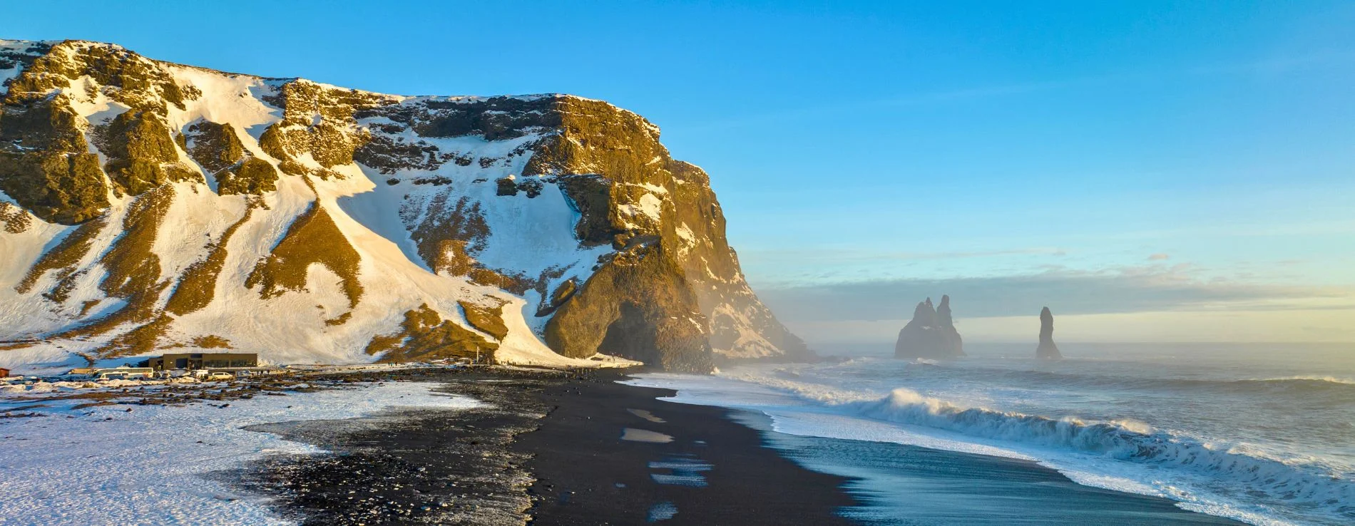 Reynisfjara black sand beach snow covered in winter with view of Sea stacks and Cave.