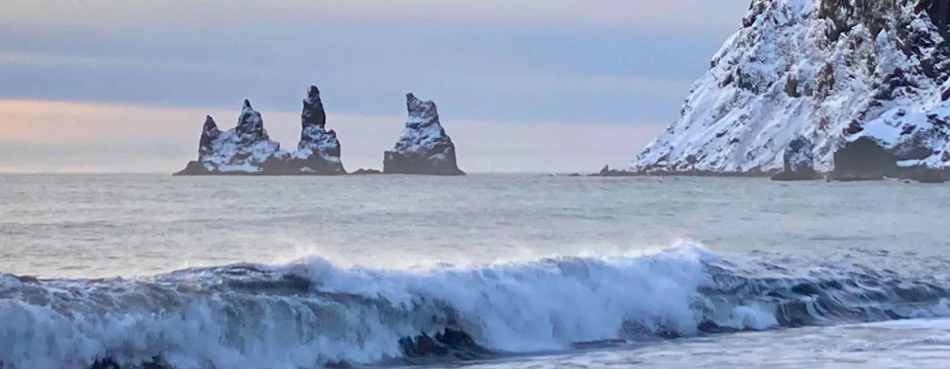 Vikurfjara black sand beach with clear view of snow covered Reynisdrangar on a winter day in Iceland.