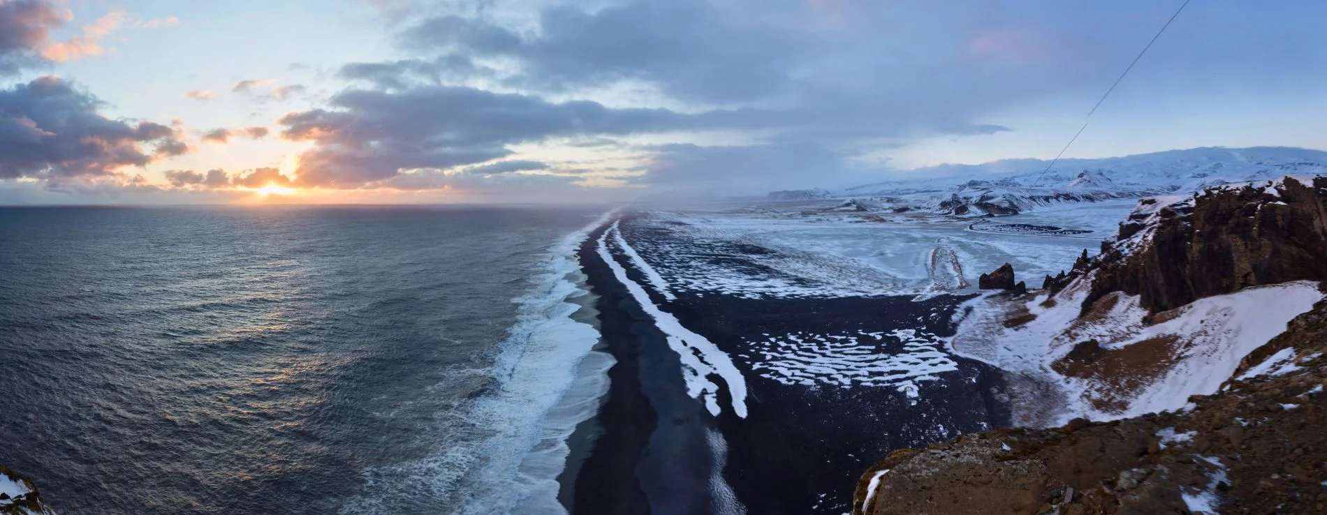 Solheimafjara Black Sand Beach Stretch in winter with snow covering the sand and a golden winter sunset in the background.