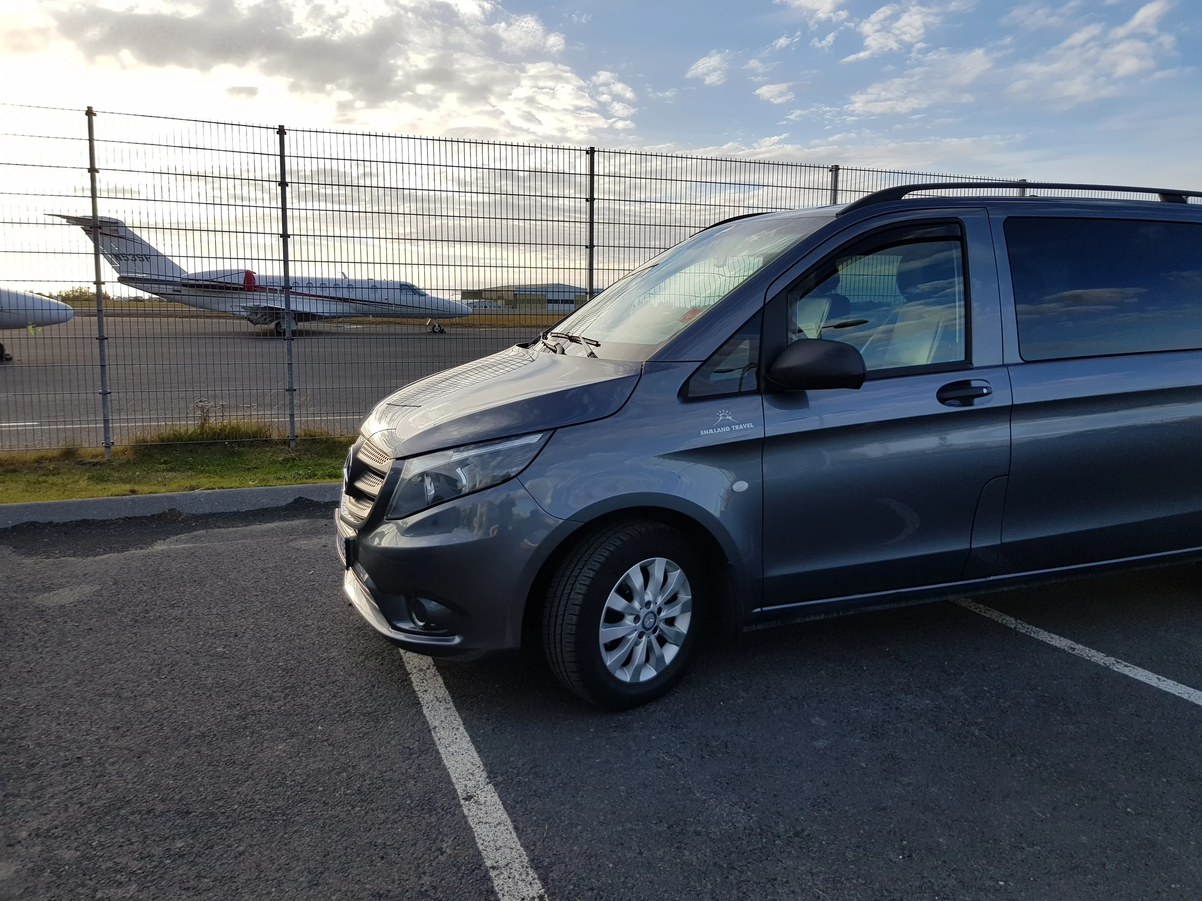Private Airport Shuttle vehicle parked with airplanes in the background.