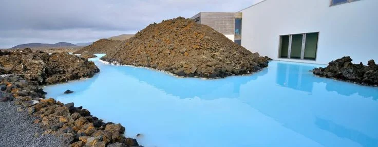 Exterior of the Blue Lagoon building with waters reaching the walls and lava rocks around.