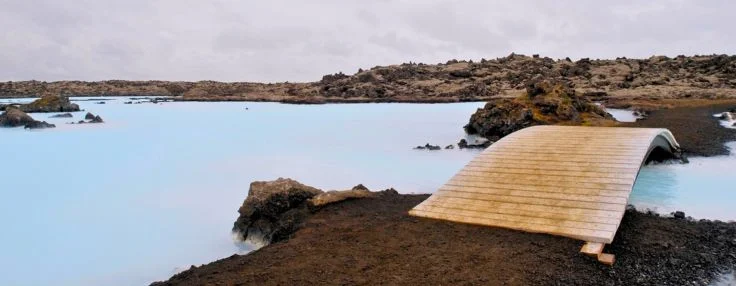 Wooden footbridge over milky water of the Blue Lagoon on a cloudy day in Iceland.