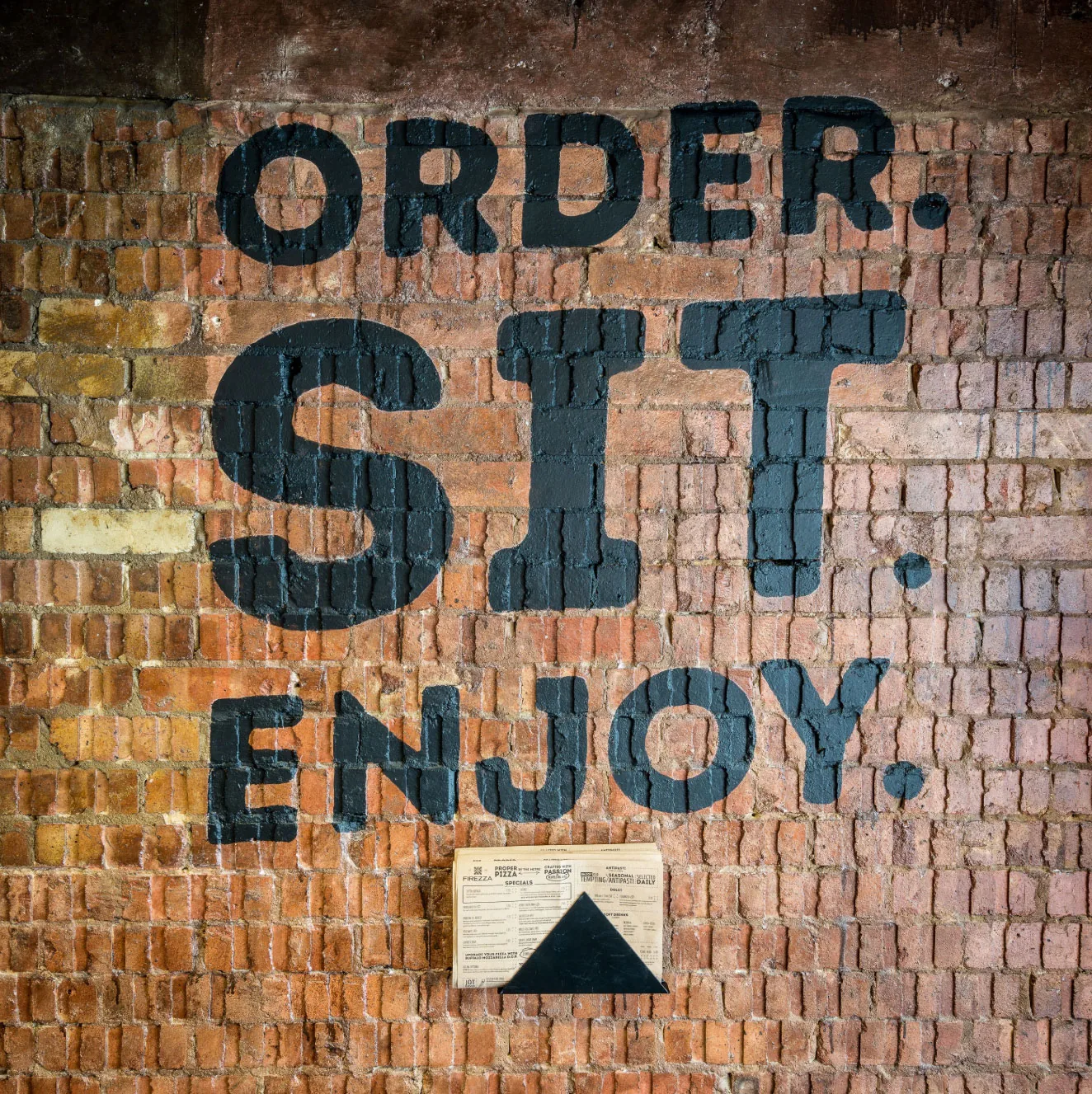 Order. Sit. Enjoy. painted in large dark letters on an exposed brick wall